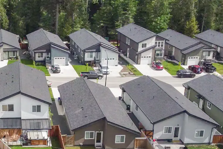 Aerial view of a suburban neighborhood developed by Little Crow Projects, featuring modern single-family homes with driveways, garages, and small green lawns, all nestled among trees in the background.