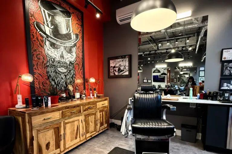 A modern barbershop with a large painting of a bearded man in a top hat, a vintage barber chair, wooden cabinets with grooming products, and mirrors reflecting the shop’s interior and lighting.